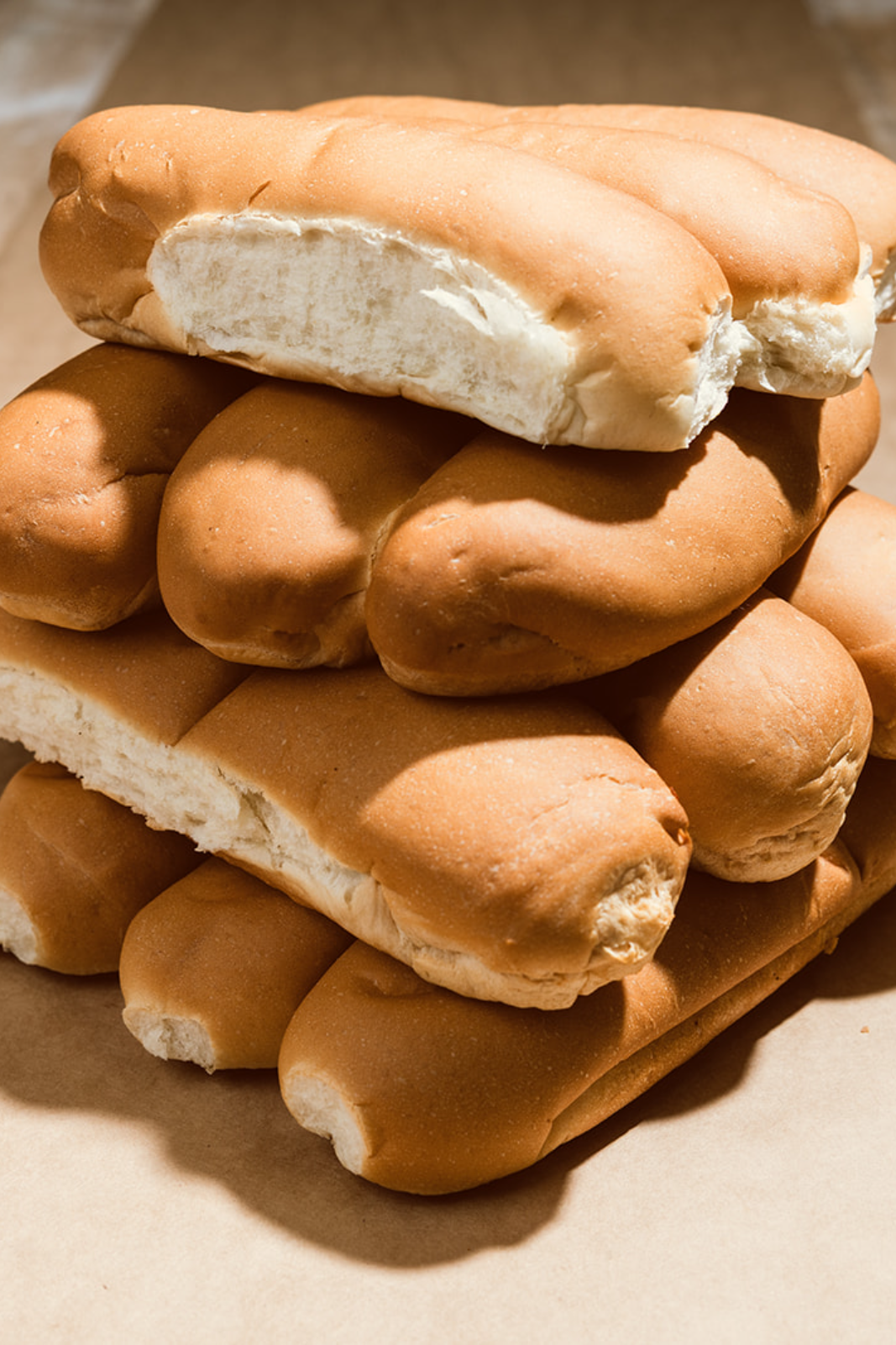 A stack of fresh 8-inch and 12-inch La Segunda hoagie rolls on brown kraft paper in warm morning light, baked that morning for Tampa Bay delivery.